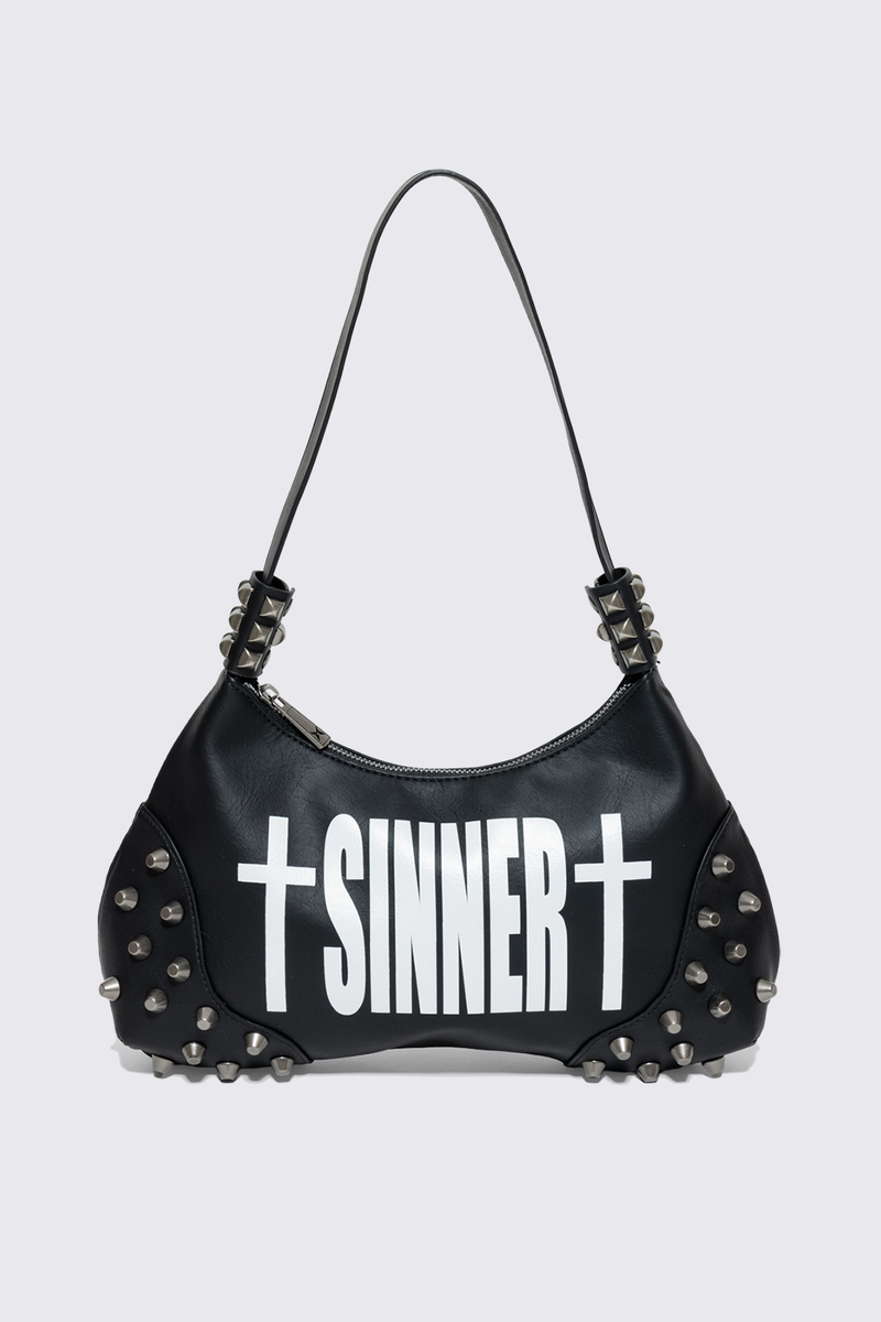 Black faux leather shoulder bag with white sinner cross print, studded panels and grunge aesthetic.