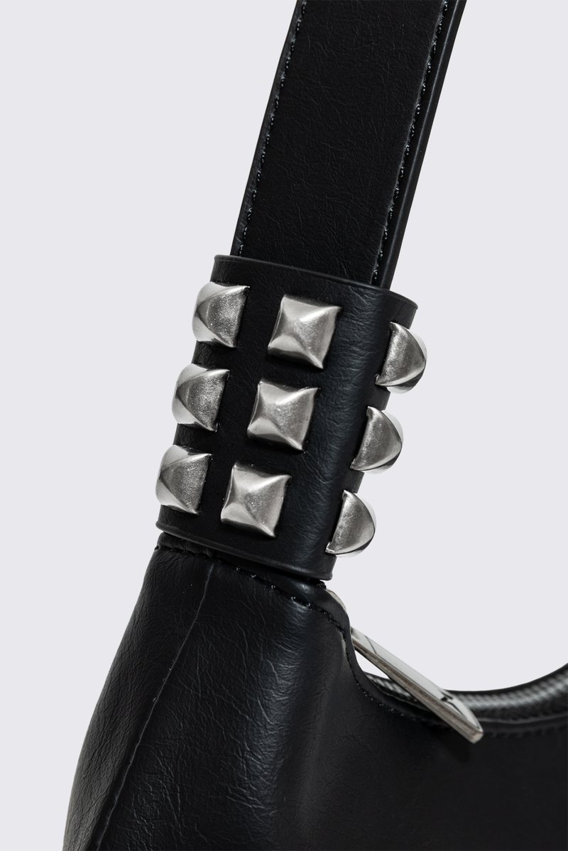 Black faux leather shoulder bag with white sinner cross print, studded panels and grunge aesthetic.
