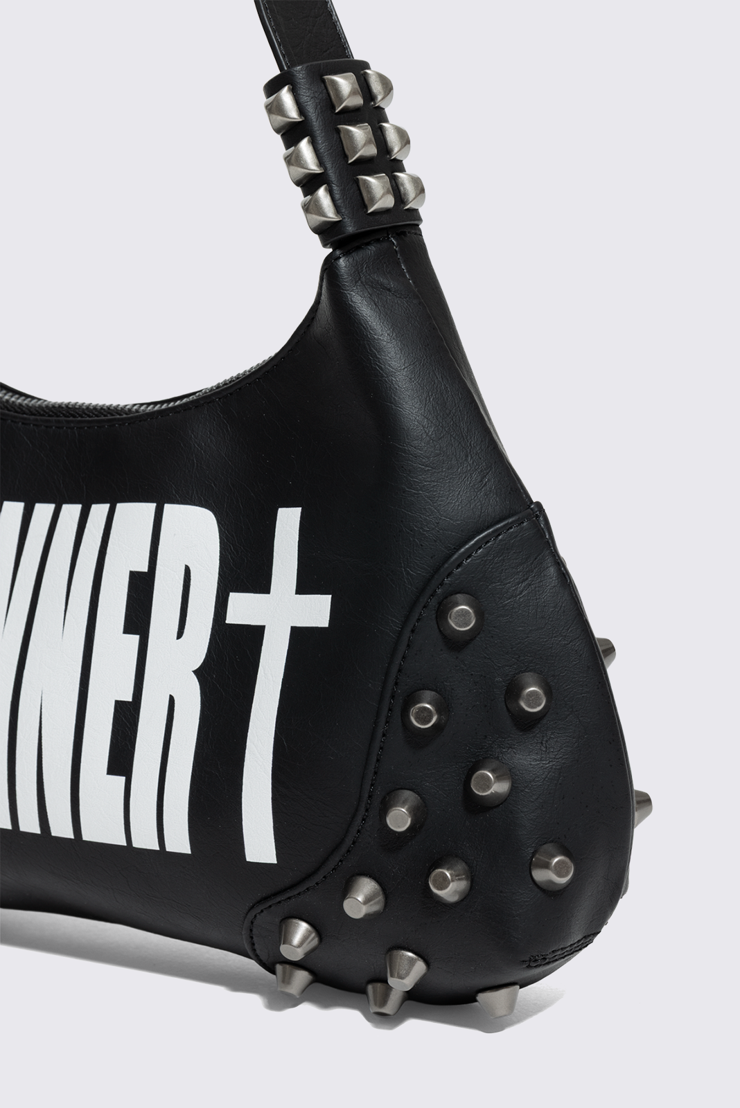 Black faux leather shoulder bag with white sinner cross print, studded panels and grunge aesthetic.