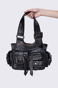 Black leather handbag with multiple pockets, buckles, and a star design, held by a hand, featuring an edgy, utilitarian style.