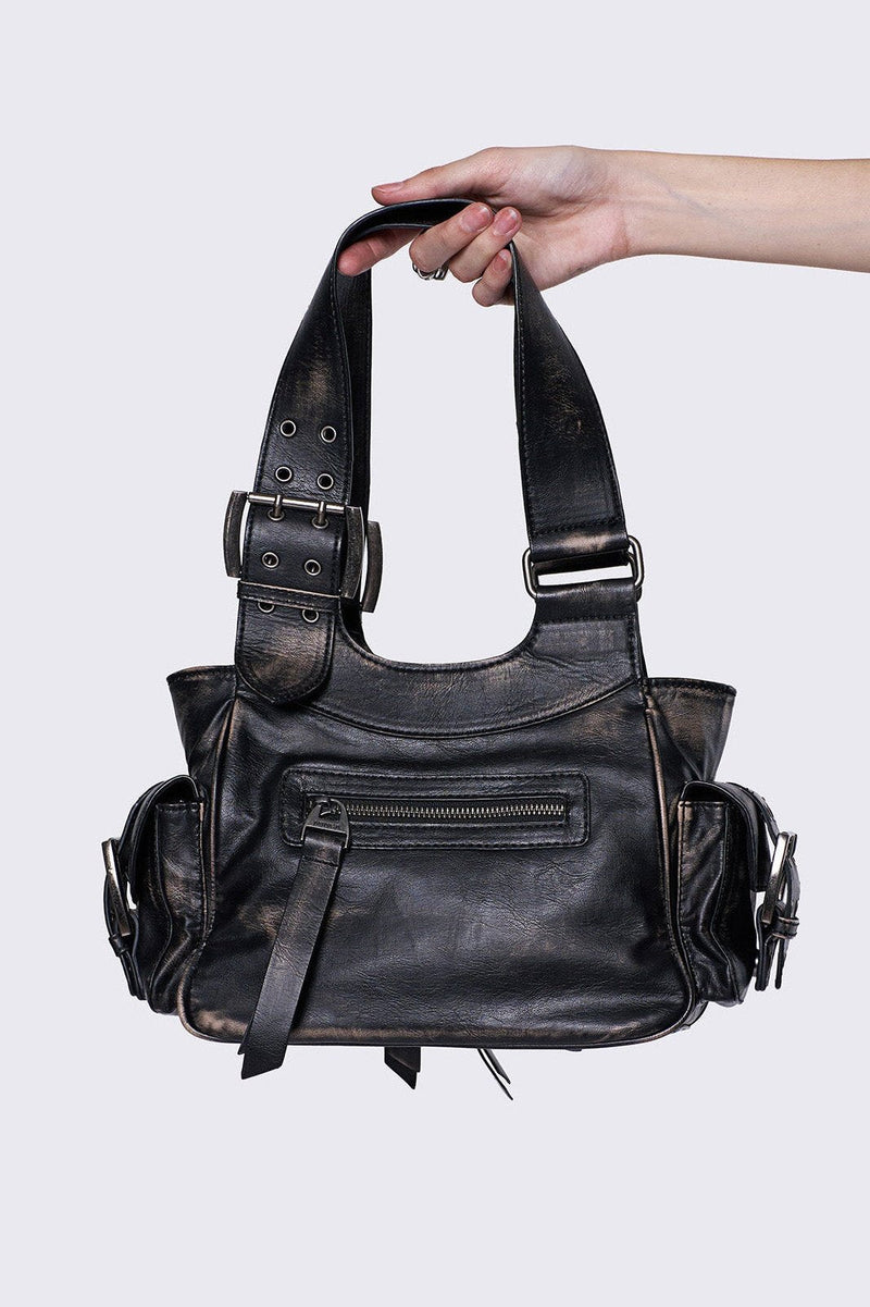 Black leather handbag with multiple pockets, buckles, and a star design, held by a hand, featuring an edgy, utilitarian style.