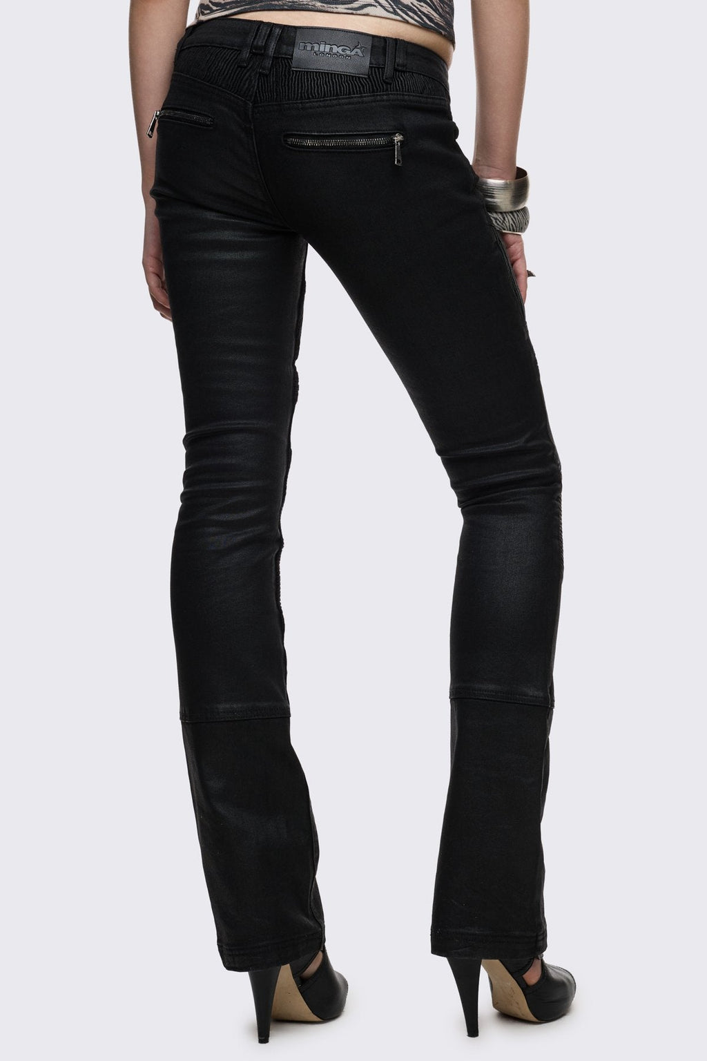 Bootcut jeans in black coated denim with ribbed paneling and zipper details, low-rise grunge aesthetic.