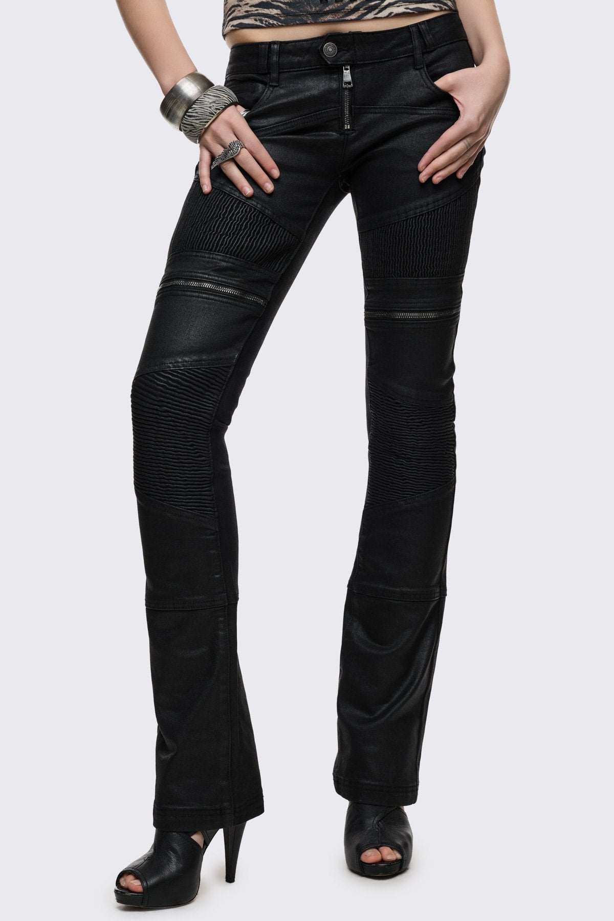 Bootcut jeans in black coated denim with ribbed paneling and zipper details, low-rise grunge aesthetic.