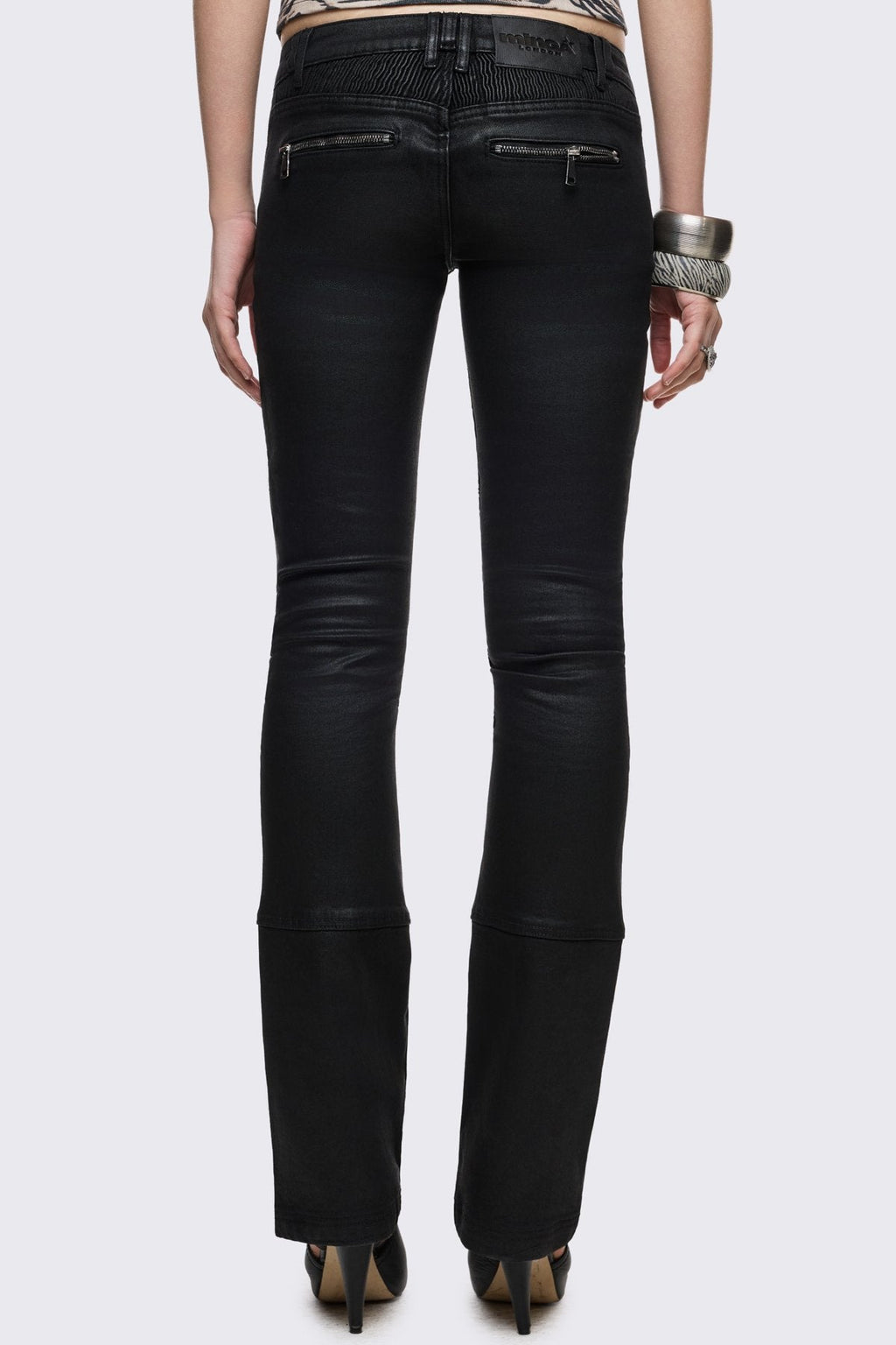 Bootcut jeans in black coated denim with ribbed paneling and zipper details, low-rise grunge aesthetic.