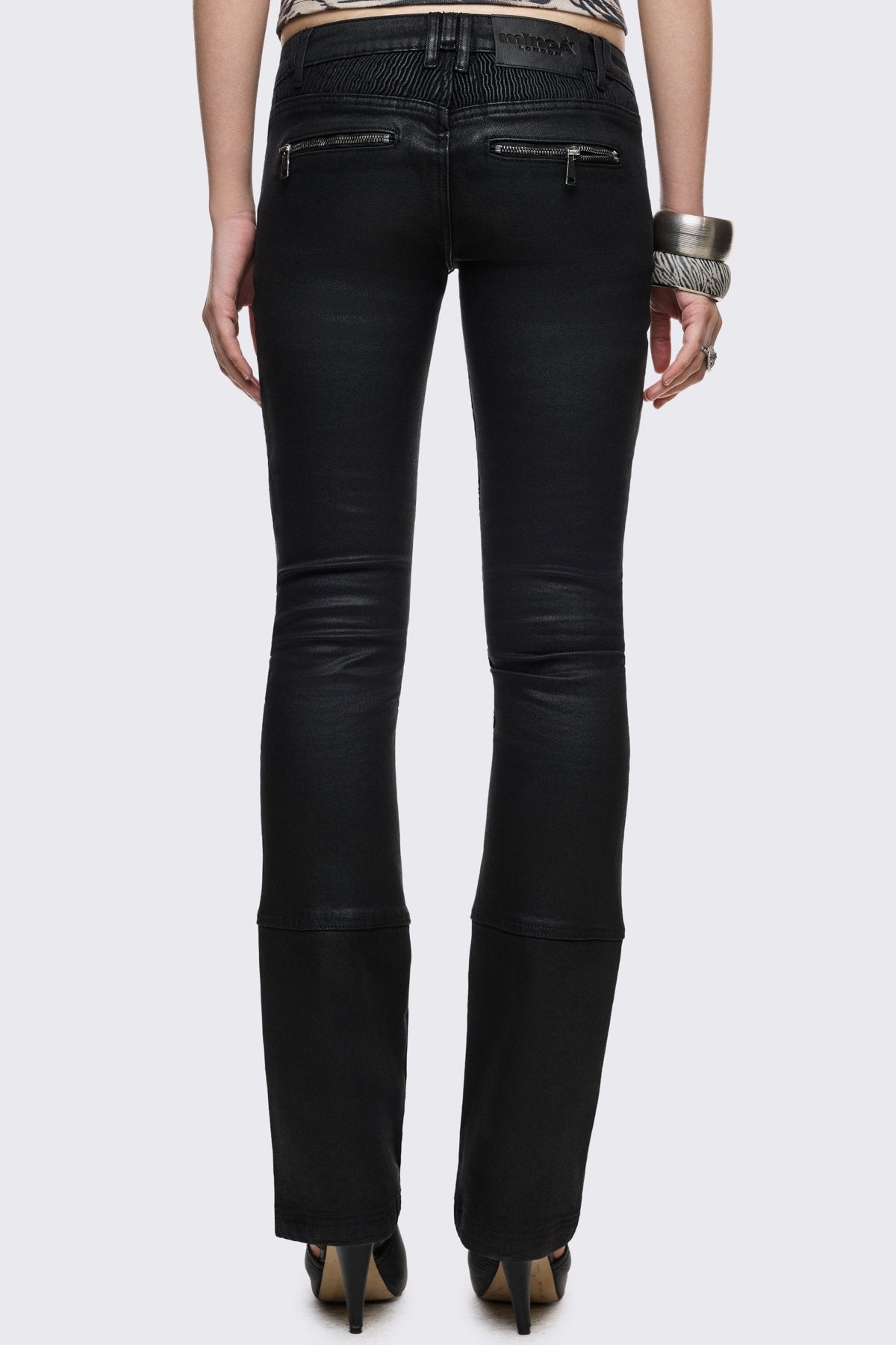 Bootcut jeans in black coated denim with ribbed paneling and zipper details, low-rise grunge aesthetic.