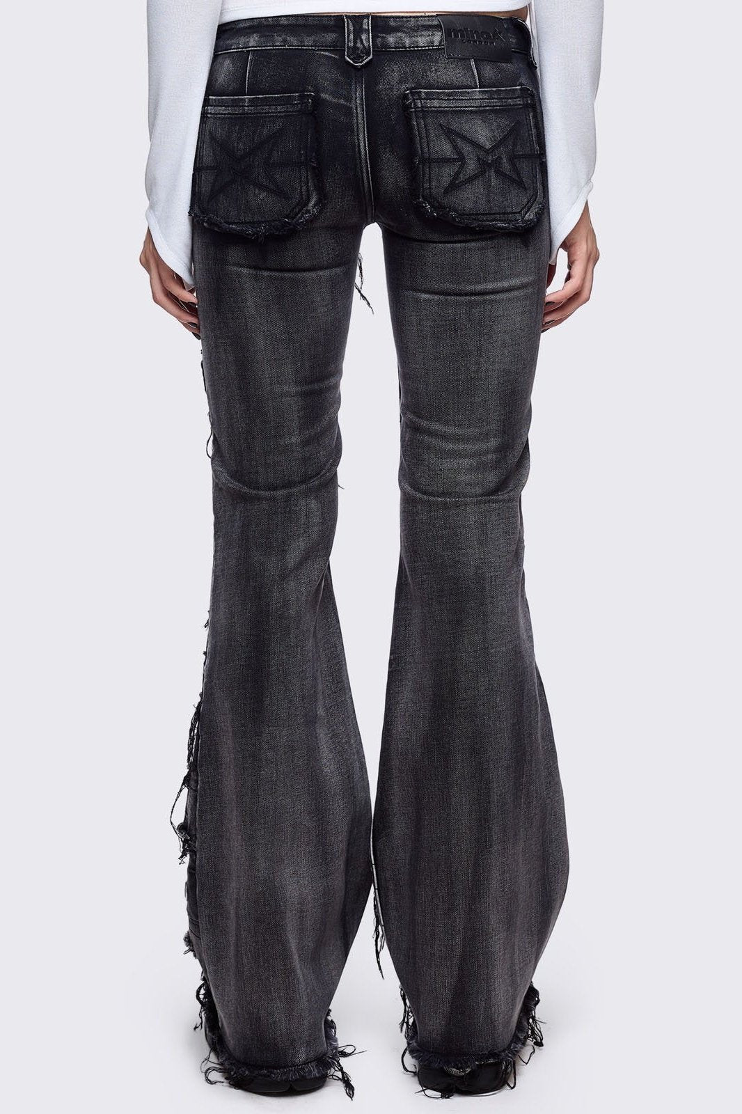 Black washed flare jeans featuring heavy distressed and shedded, eyelet, piercing and stud details. 
