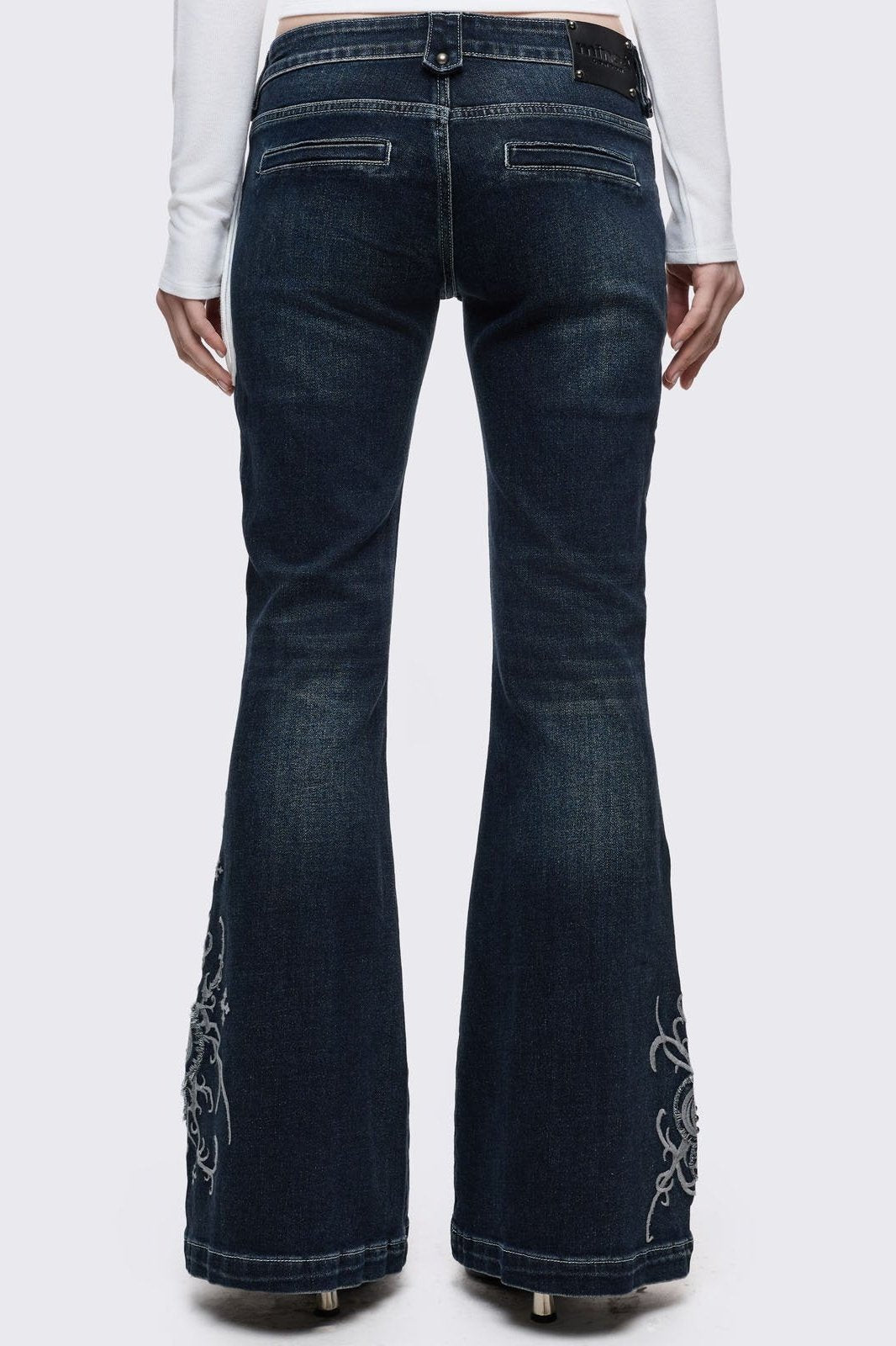 Dark blue wash flared jeans featuring gothic floral and fleur-de-lis embroidery on the lower legs and seams details. 