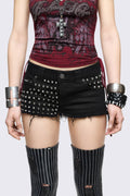 Black denim hot pants with silver spikes, raw frayed hems and low-rise fit in a grunge Y2K style.