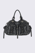 Black acid-wash denim shoulder bag with studs, ruched pockets and buckle details in a grunge Y2K style.